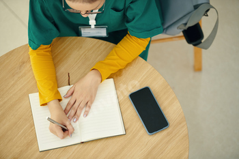 Nurse Writing in Notebook at Wooden Table