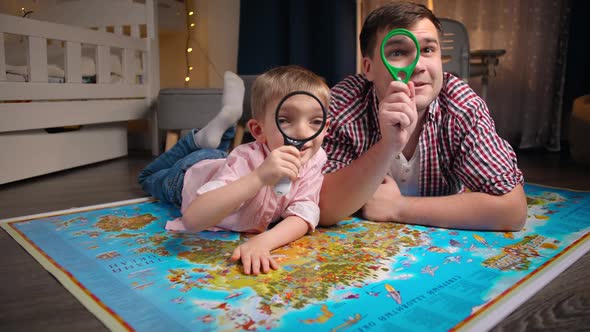 Happy Little Boy with Father Lying on Big Map and Looking Through Magnifying Glass