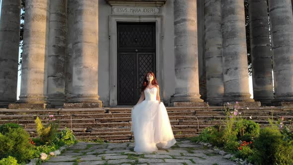 Happy Bride Spins Around Herself Raising Her Wedding Dress Against the Background of an Old Church