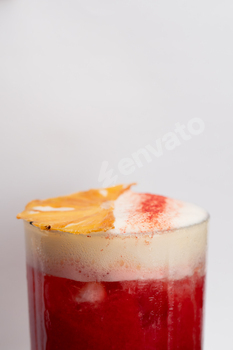 close-up on a white background stands a glass glass with foamy red cocktail drops on the glass an