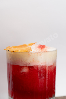 close-up on a white background stands a glass glass with foamy red cocktail drops on the glass an