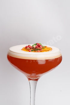 close-up on a white background stands a glass glass with foamy red cocktail drops on the glass an