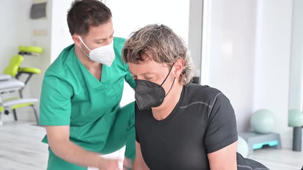 Therapist with Protective Face Mask Assisting Patient With Stretching Exercises