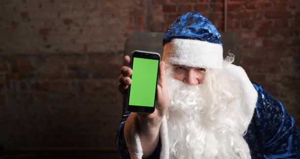 Santa Claus in Blue Costume Shows Mobile Phone with Green Screen in His Hand
