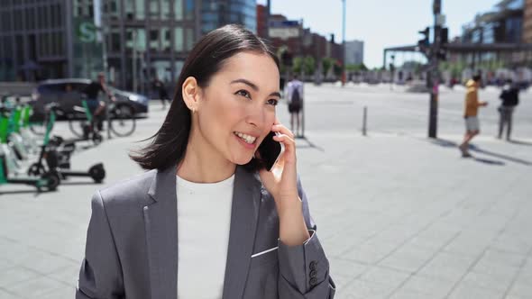 Young Happy Asian Woman Talking on Cellphone Standing on Big City Street