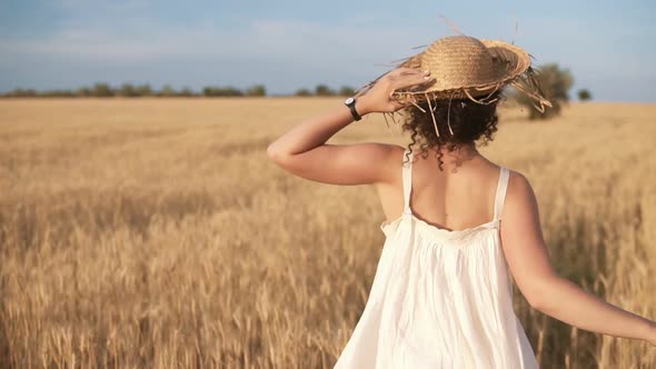 Tracking Footage of a Beautiful Girl in White Summer Dress and Straw Hat Running Freely By Wheat