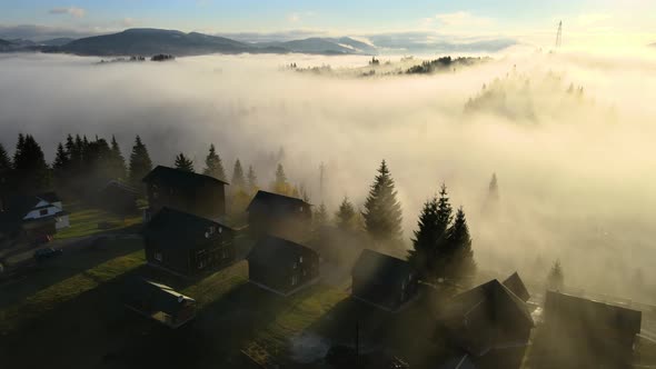 Aerial view of a village houses on hill top in autumn foggy mountains at sunrise