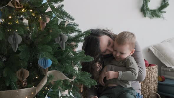 Woman Sitting with Little Son Near Christmas Tree