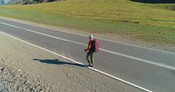 Flight Over Hitchhiker Tourist Walking on Asphalt Road. Huge Rural Valley at Summer Day. Backpack