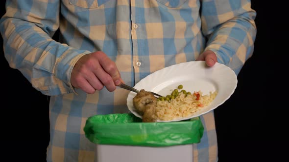 Man Scraping with a Plate a Chicken Leg, Rice, Green Peas Into Garbage Bin