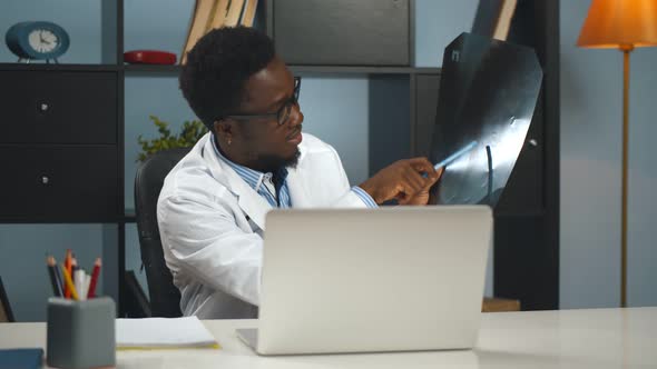 Afro-american Male Doctor Working From Home and Showing X-ray To Patient Online