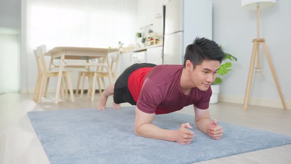 Asian handsome active man doing plank exercise on floor in living room.