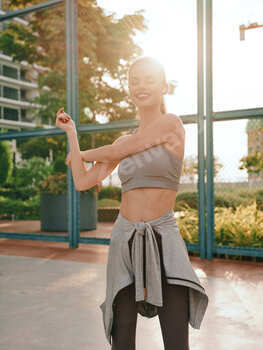 Young woman stretching outdoors in athletic wear with a confident smile, sunlight creating a warm