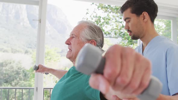 Male physiotherapist looking at senior man exercising with dumbbells in retirement home