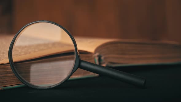 Girl Turns the Page of an Old Book Next to a Magnifying Glass