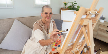 Smiling elderly woman painting colorful flowers on canvas