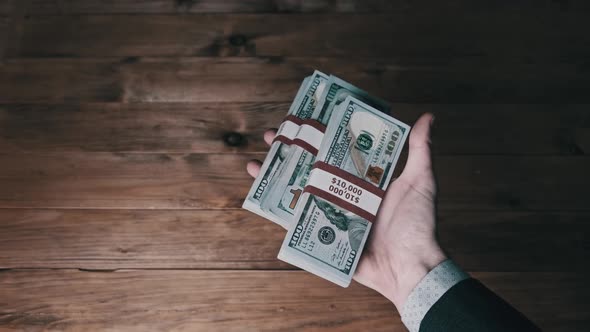 Male Hand Hold Three Stacks of 10000 US Dollar Bills on Wooden Background