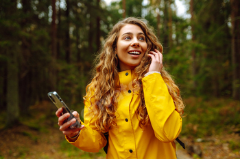 Travel apps. Curly young woman traveler in yellow coat holding smartphone in hand. Concept of travel