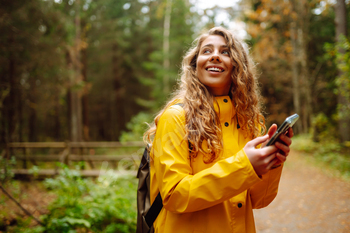 Travel apps. Curly young woman traveler in yellow coat holding smartphone in hand. Concept of travel