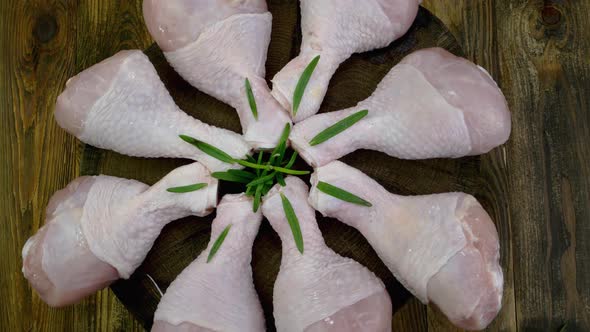 Fresh raw chicken drumsticks with rosemary twigs rotating slowly on turntable.