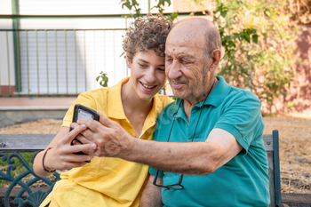 Grandson teaching grandfather to use smartphone, intergenerational bonding outdoors