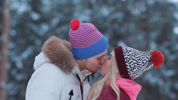 Lovely Happy Guys Enjoying Time Together. Couple in Knit Hats Hugs and Kisses in Winter Forest