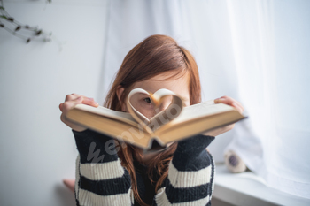 A girl is holding a book. Heart-shaped pages. Reading, Knowing, Learning