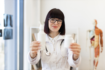 Smiling female doctor holding medication bottles in medical office