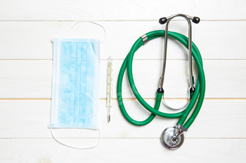 Top view of stethoscope, protective mask and mercury thermometer