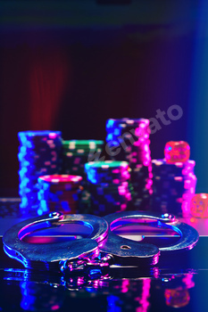 Silver Handcuffs Resting on Laptop Keyboard With Poker Chips.