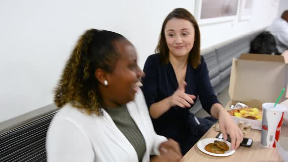 Caucasian woman telling a joke and laughing while eating lunch with African American friend