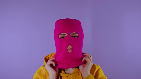 Close Up Young Woman Puts on Pink Balaclava on Purple Background
