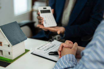 Home loan officer uses a calculator to calculate with a house plan.