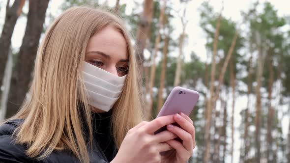 Young Blond Woman Wearing Protective Mask Talking on Phone Outside in the Park