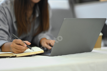 Young female freelancer working with laptop and writing in a notebook