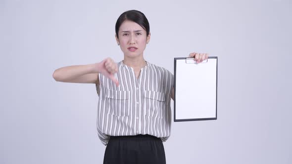 Stressed Asian Businesswoman Showing Clipboard and Giving Thumbs Down