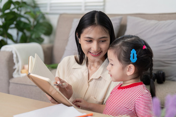 Asian mother teaching daughter with notebook in cozy living room