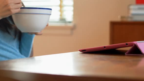 Woman having cereal while using digital tablet