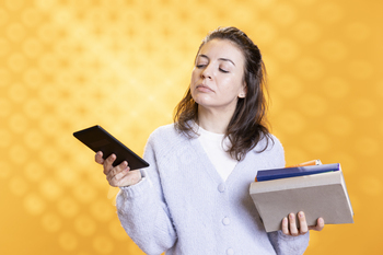 Woman holding stack of textbooks and ebook reader, studio background