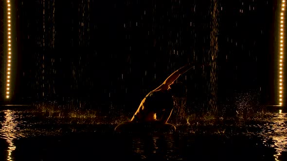 Silhouettes of a Slender Woman Who Practices Yoga Exercises. Raindrops Are Falling From the Ceiling