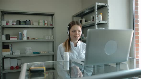 Portrait of Female Pharmacist Online Consultant in Headset with Pills Jar Speak