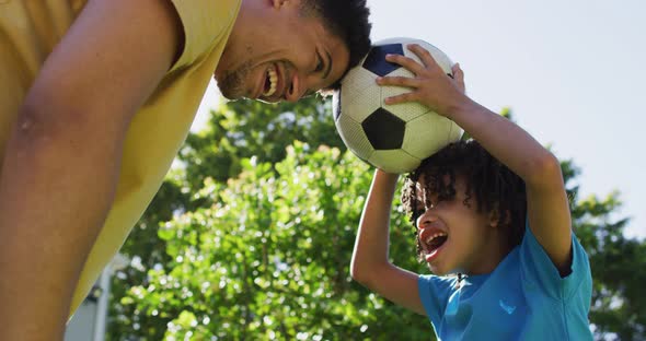 Happy biracial man and his son playing football in garden