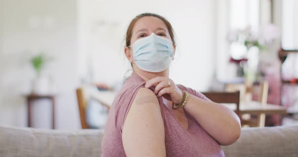 Caucasian woman wearing face mask pointing at bandage on her arm