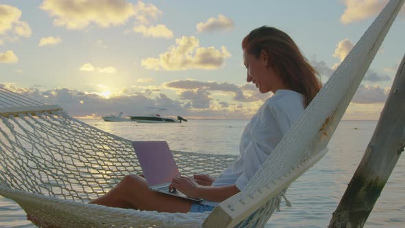 A Young Woman Entrepreneur Uses a Laptop to Work on the Hammock at Ocean