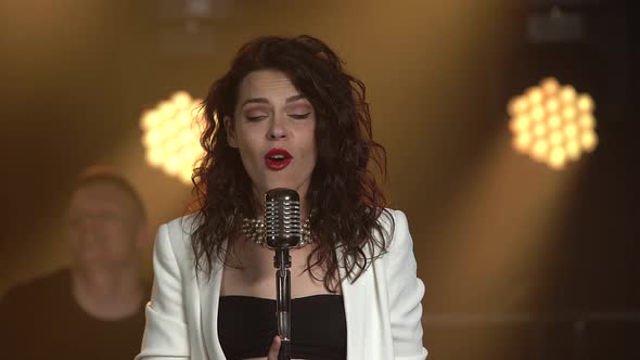 A Stylish Girl Vocalist Sings on Stage in a Vintage Microphone. Dark Studio with Smoke and Neon