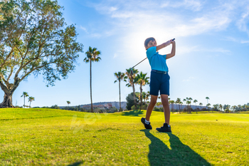 Boy swinging golf alone in a course