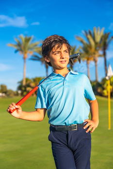 Boy carrying a gold club along a course