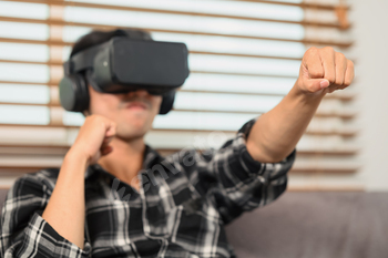 Excited man with VR headset playing boxing game and throwing punches in the air