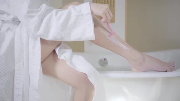 Unrecognizable Woman Shaving Slender Legs with Razor. Side View of Young Caucasian Lady Depilating