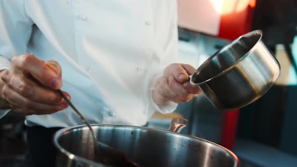 The chef makes sauce in a saucepan in professional restaurant kitchen process of food preparation